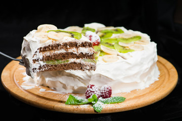 selective focus on a piece of delicious cake with bananas and kiwi. On the dark background tasty cake