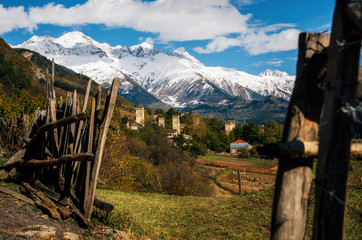 View of the Svanetian towers in Mestia village against mountains with glaciers snow peaks through the fence. Upper Svaneti Georgia. Georgian landmark