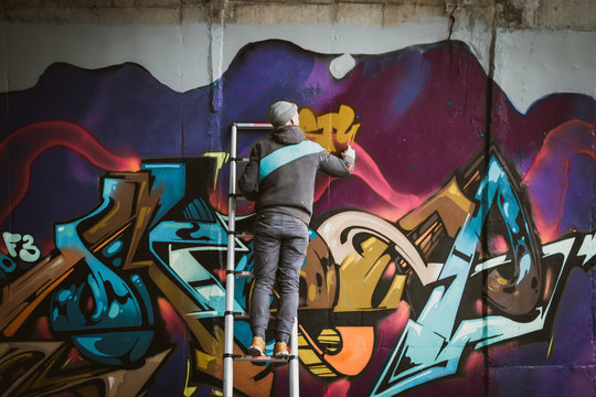 Graffiti artist standing on ladder and painting with aerosol spray on the wall