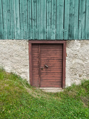 Close up view of old wooden door with green grass below and rough wooden structure above.