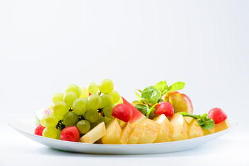 classic summer Italian food. Beautifully decorated fruit platter with watermelon, melon, apricot and grapes on a white plate, light background