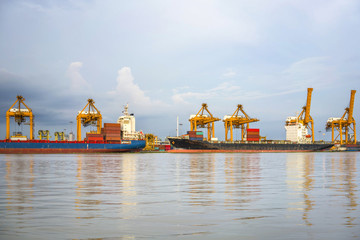Shipping port, Container Cargo freight ship with working crane loading bridge in shipyard at dusk for Logistic Import Export in Bangkok (With blur trademark, brand, logo.) 