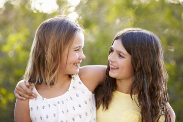 Fototapeta premium Portrait of two smiling young girls looking at each other outdoors