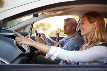 Naklejka premium Young couple on a trip in a car navigating with a smartphone