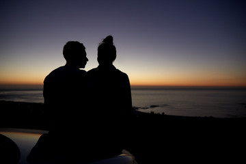 Couple relaxing by the sea at sunset by a car, silhouette