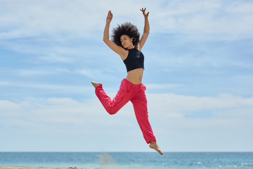 Young pretty sportswoman jumping on beach raising hands