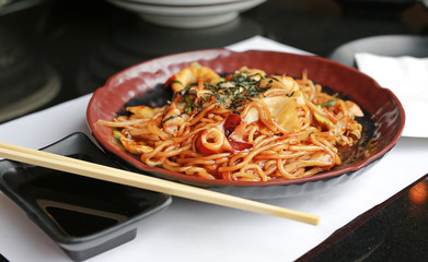 Japanese yakisoba noodles in brown ceramic plate on the black table.