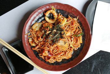 Japanese yakisoba noodles in brown ceramic plate on the black table.