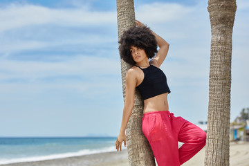 Beautiful afro american woman leaning against palm on beach