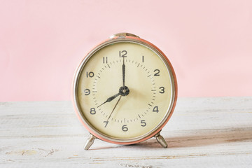 Retro alarm-clock on wooden and pink background. Copy space.
