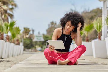 Afro american woman sitting crossed legs outside using tablet