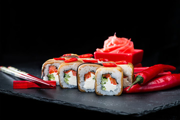 Traditional Japanese cuisine.  Selective focus on set of sushi rolls with salmon, cream cheese, rice, chili pepper and cucumber on dark background, near ginger and chili pepper