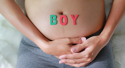 Close up Pregnant woman sitting on soft sofa and touching her belly with sign BOY in front of her belly.