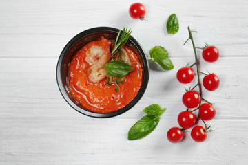 Plastic container with delicious shrimps in tomato sauce on wooden table