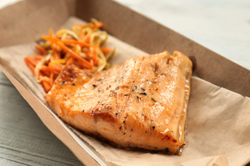 Cardboard box with delicious fish and vegetables on table