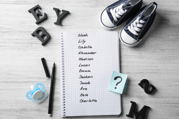 Composition with list of baby names in notebook on wooden background