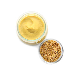 Mustard seeds in bowl and jar with delicious sauce on white background