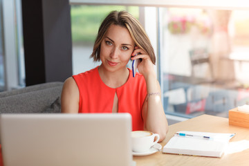 Cheerful business woman in the cafe talking by mobile phone