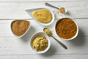 Mustard seeds, powder and sauces in dishes on wooden table