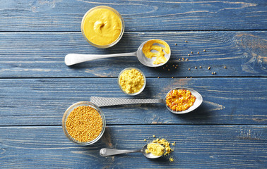 Mustard powder, seeds and sauces in dishes on wooden table