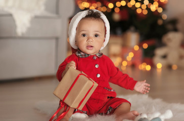 Cute little baby with Santa hat and gift box in decorated for Christmas room