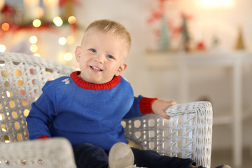 Cute little boy sitting in wicker chair on blurred background