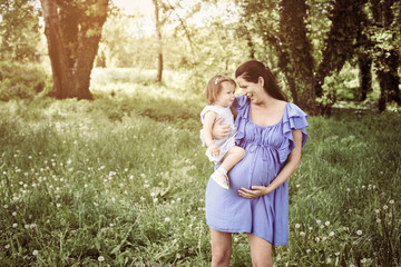 Pregnant mother playing with little daughter in park. Mother and daughter in nature.