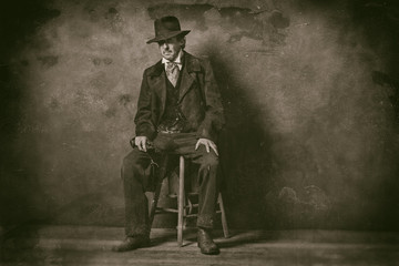 Classic wet plate photo of vintage 1900 western mature man with revolver sitting on wooden stool.