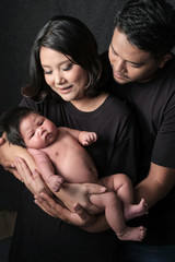 family portrait of young asian mum and dad and boy newborn in black background .