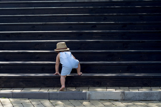 The one-year child climbs up the stairs. Cute baby boy in hat plays on the stairs. The concept of happy childhood. Nature, outdoors, summer