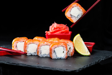 traditional Japanese cuisine. Process of eating sushi rolls with salmon, cream cheese, rice and lime on dark background, selective focus