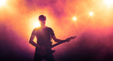 Silhouette of guitar player on stage on orange background with smoke and spotlights