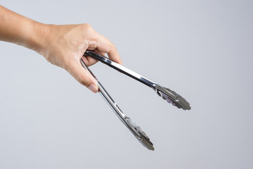 Hand holding silver serving kitchen tongs for picking food