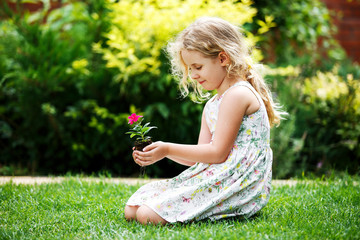 Little blonde girl holding young flower plant in hands on green background.