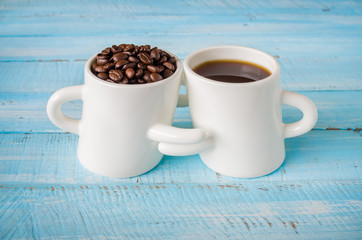 Two cup of hot coffee and roast seeds coffee  on wooden background.