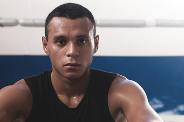 Fototapeta na wymiar Portrait of sweaty latin american male boxer looking at camera confidently after working out in boxing gym