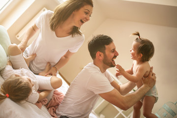 Family spending free time at home. Cheerful family having fun with their daughters on  the bed.