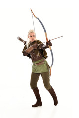 full length portrait of a blonde girl wearing green and brown medieval costume, holding a bow and...