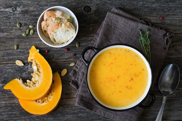 Pumpkin cream soup in bowl on rustic wooden table. Top view, copy space for text