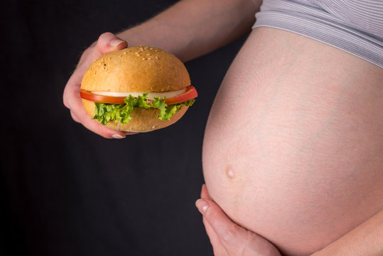 A pregnant woman with belly holding a burger. Concept of fast food and unhealthy eating during pregnancy