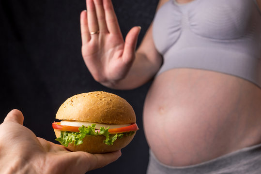 Pregnant woman with belly refuses from the burger. The concept control during pregnancy weight