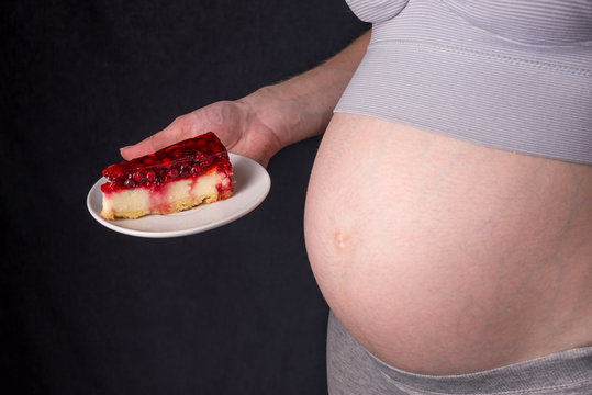 A pregnant woman with belly holding a piece of cheesecake. Concept weight control and an unhealthy diet during pregnancy