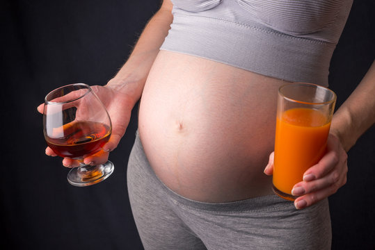Pregnant woman belly holding alcohol and juice in hands. Concept choice for a healthy lifestyle during pregnancy