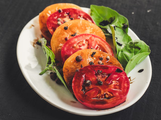 Salad of slices of tomatoes with basil and spices in a white plate. Black background.