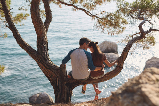 romantic young couple in love together. Happy young couple in love sitting and kissing on a tree branch on sea in background