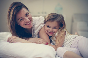Mother with her cute little daughter lying on bed.
