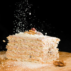 close-up delicious cake of puff pastry with sour cream and walnut sprinkled crumbs on a wooden plate on dark background