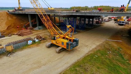 Bridge construction drone view. Sky view of crawler crane repair bridge over highway road. Dron view of new bridge construction over suburban road. Aerial view of bridge repair on highway road - Powered by Adobe