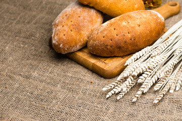 homemade rustic wheat breads on a wooden cutting board, near the wheat. Selective focus, rustic style