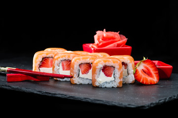 Traditional Japanese cuisine. Selective focus on sweet sushi rolls with salmon, cream cheese, rice and strawberry on dark background, near strawberries and ginger